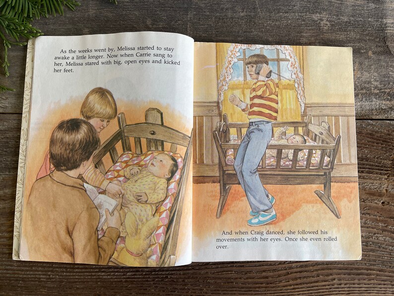 Pu&ograve; includere: Un'illustrazione di un libro per bambini che mostra un bambino in una culla con due fratelli maggiori. Il bambino sta guardando il fratello maggiore che tiene un libro. L'altro fratello &egrave; in piedi dietro la culla. Il testo sulla pagina dice: "Con il passare delle settimane, Melissa ha iniziato a rimanere sveglia un po' pi&ugrave; a lungo. Ora, quando Carrie le cantava, Melissa la fissava con occhi grandi e aperti e calciava con i piedi. E quando Craig ballava, lei seguiva i suoi movimenti con lo sguardo. Una volta, si &egrave; persino rotolata."