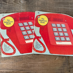 May include: Two vintage children's books shaped like red telephones. Each book features a red telephone illustration with a blue background and the text "The Telephone Book". The books are designed to teach children about telephones.