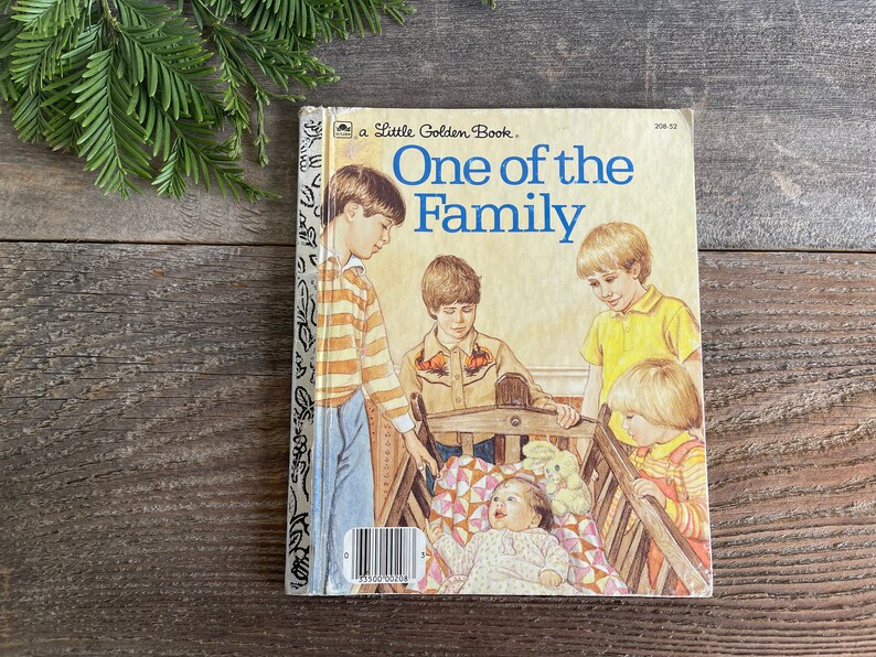 Pu&ograve; includere: Un libro vintage della serie Little Golden Book intitolato "One of the Family". La copertina presenta una famiglia di bambini, tra cui un bambino in una culla, con una combinazione di colori giallo, marrone e blu.