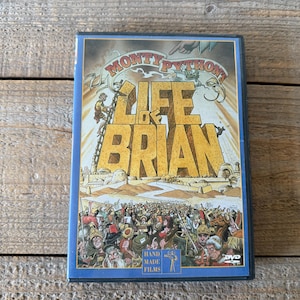 Peut inclure: Boîtier DVD du film "La Vie de Brian" des Monty Python. La couverture présente le titre du film en grandes lettres jaunes, avec une foule de personnes en bas. Le boîtier est bleu et porte le logo DVD.