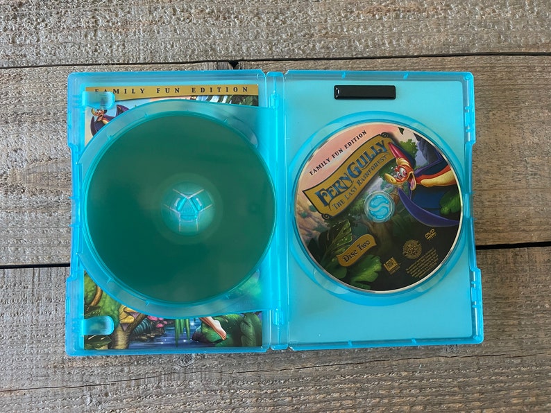 Op de afbeelding: Een blauwe DVD-doos met een afbeelding van een cartoonvogel op de voorkant. De doos is open en de DVD is zichtbaar. De DVD is gelabeld met "FernGully: The Last Rainforest" en "Disc Two".