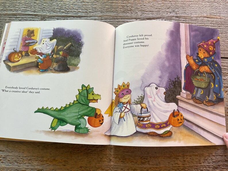 May include: A children's book illustration showing a group of characters dressed in costumes for Halloween. The characters include a dinosaur, a ghost, a princess, and a bear. The text in the image reads "Everybody loved Corduroy's costume. "What a creative idea!" they said. Corduroy felt proud. And Puppy loved his dinosaur costume. Everyone was happy!"