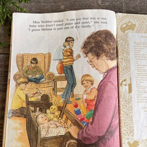 Pu&ograve; includere: Un'illustrazione colorata di una famiglia in una casa. Una donna sorride e tiene una bambola in una culla. Ci sono tre bambini che giocano con i giocattoli nella stanza. Il testo dell'immagine dice: "Miss Webber sorrise. "Posso vedere che questo &egrave; un bambino che non ha bisogno di pace e tranquillit&agrave;", disse. "Immagino che Melissa sia solo uno della famiglia."