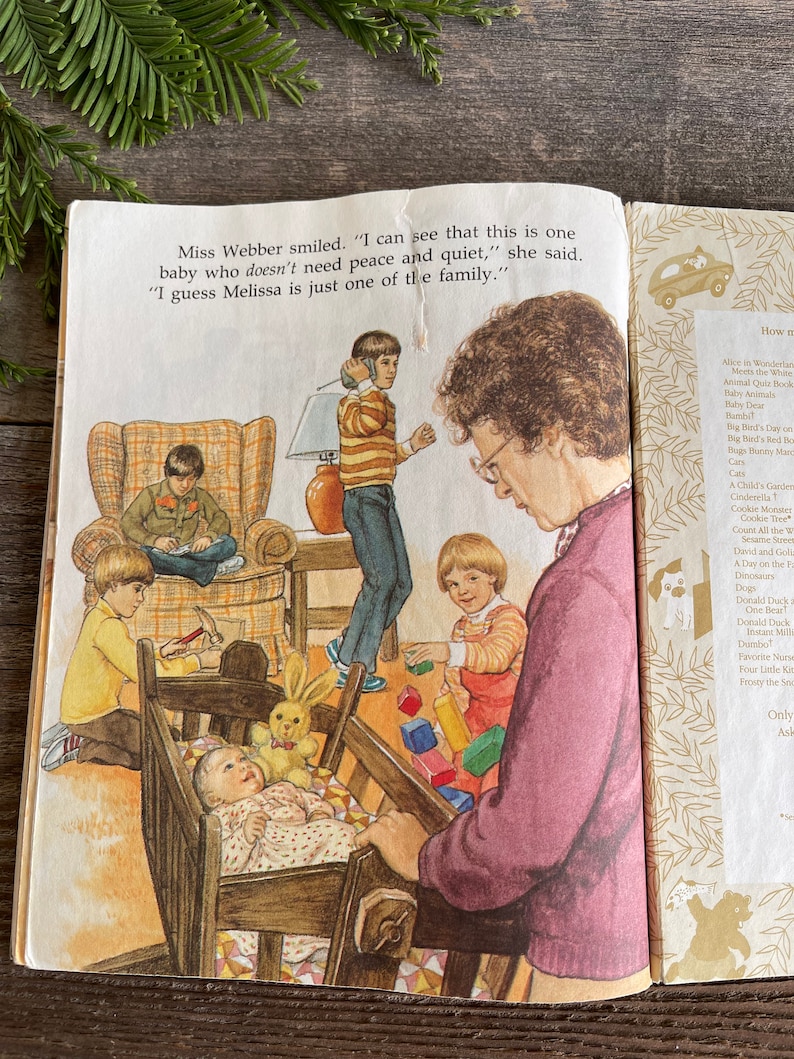 Pu&ograve; includere: Un'illustrazione colorata di una famiglia in una casa. Una donna sorride e tiene una bambola in una culla. Ci sono tre bambini che giocano con i giocattoli nella stanza. Il testo dell'immagine dice: "Miss Webber sorrise. "Posso vedere che questo &egrave; un bambino che non ha bisogno di pace e tranquillit&agrave;", disse. "Immagino che Melissa sia solo uno della famiglia."
