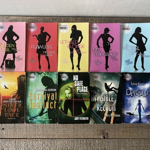 Puede incluir: Una colección de diez libros de bolsillo con cubiertas coloridas. Los libros presentan títulos como "Golden Girl", "Flawless" y "Survival Instinct". Cada cubierta muestra una silueta de mujer y el nombre del autor.