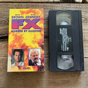 May include: A VHS tape of the movie "FX: Murder by Illusion" starring Bryan Brown and Brian Dennehy. The cover features a fiery background with portraits of the actors.