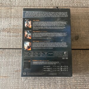 K&ouml;nnte beinhalten: Ein DVD-Box-Set mit der Die Hard-Film-Trilogie. Die Box ist schwarz mit silbernem Rand und zeigt Bilder von Bruce Willis als John McClane aus jedem Film. Die R&uuml;ckseite der Box enth&auml;lt eine Beschreibung jedes Films und eine Liste der besonderen Merkmale.
