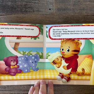 Puede incluir: Doble p&aacute;gina de un libro infantil con Daniel Tigre sosteniendo un beb&eacute; tigre. A la izquierda, un oso de peluche morado y un elefante azul con lunares blancos. Las burbujas de texto contienen di&aacute;logo.