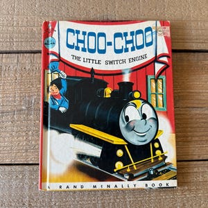 Puede incluir: Libro infantil vintage titulado "Choo-Choo The Little Switch Engine" de Rand McNally. La portada presenta un tren de dibujos animados sonriente con un cuerpo negro, detalles amarillos y una cara amigable. El fondo es rojo.
