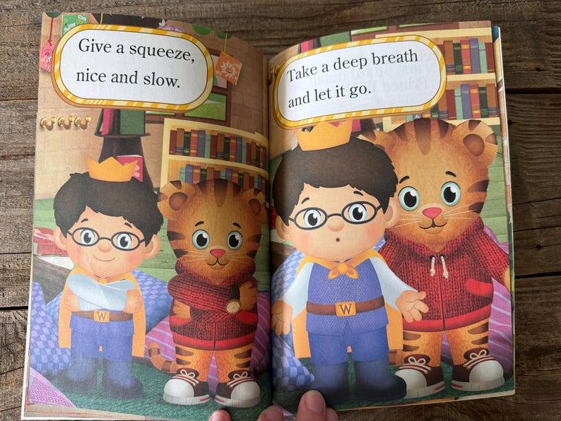 May include: A children's book illustration featuring two cartoon characters, one a boy wearing glasses and a crown, and the other a tiger. Text bubbles read "Give a squeeze, nice and slow" and "Take a deep breath and let it go."