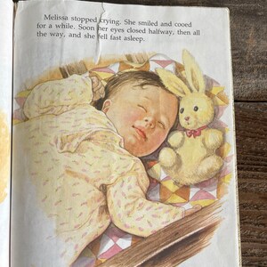 Pu&ograve; includere: Una bambina dorme profondamente in una culla con una trapunta a motivi gialli e rosa. Indossa un body con stampa floreale giallo e rosa e ha un coniglietto di peluche accanto a lei.