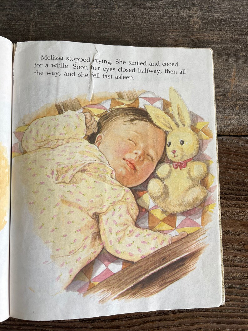 Pu&ograve; includere: Una bambina dorme profondamente in una culla con una trapunta a motivi gialli e rosa. Indossa un body con stampa floreale giallo e rosa e ha un coniglietto di peluche accanto a lei.
