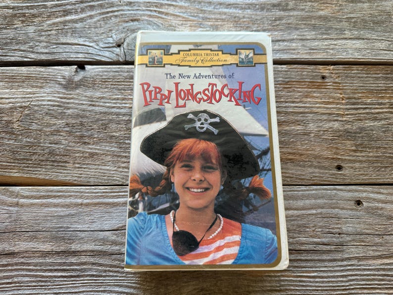 May include: A VHS tape of "The New Adventures of Pippi Longstocking" from the Columbia TriStar Family Collection. The cover features a smiling girl with red hair wearing a pirate hat. The background shows a ship and blue sky.