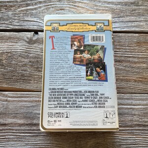 May include: A VHS tape for "The New Adventures of Pippi Longstocking" from Columbia Pictures. The cover features images from the film and the Columbia Tristar Family Collection logo. The tape is on a wooden surface.