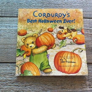 May include: A children's book cover featuring a brown teddy bear holding a large orange pumpkin. The book title is "Corduroy's Best Halloween Ever!" and is based on the character created by Don Freeman. The book is illustrated by Lisa McCue.