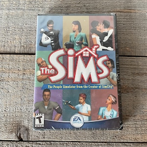 May include: The Sims video game box cover features a colorful collage of characters and the game title "The Sims" in large, bold letters. The tagline "The People Simulator from the Creator of SimCity" is printed below the title. The ESRB rating "TEEN" is displayed in the lower left corner.