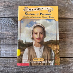 May include: A book titled "My America: Season of Promise, Elizabeth's Jamestown Colony Diary." The cover features a portrait of a young person in colonial attire. The author's name, Patricia Hermes, is visible.
