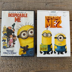 May include: Two DVD cases of the animated movie "Despicable Me" and "Despicable Me 2". The first case features a yellow minion with large goggles and the movie title. The second case features two minions and the movie title.