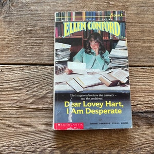 May include: A paperback book titled "Dear Lovey Hart, I Am Desperate" by Ellen Conford. The cover features a young woman sitting at a desk surrounded by books, looking stressed.