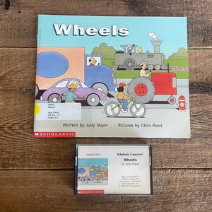 Peut inclure: Un livre et une cassette audio Scholastic intitulés "Wheels" par Judy Nayer. La couverture du livre présente des illustrations colorées de véhicules, notamment un train, une voiture, un vélo et un camion de pompiers. La couverture de la cassette audio présente une illustration similaire d'un train, d'une voiture et d'un vélo.