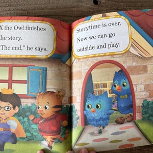May include: Open book with colorful illustrations. Text reads "X the Owl finishes the story. 'The end,' he says." and "Storytime is over. Now we can go outside and play." Features cartoon characters, including a tiger, owl, and a boy with a crown.