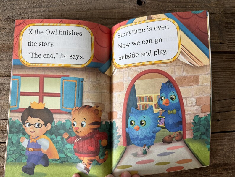 May include: Open book with colorful illustrations. Text reads "X the Owl finishes the story. 'The end,' he says." and "Storytime is over. Now we can go outside and play." Features cartoon characters, including a tiger, owl, and a boy with a crown.
