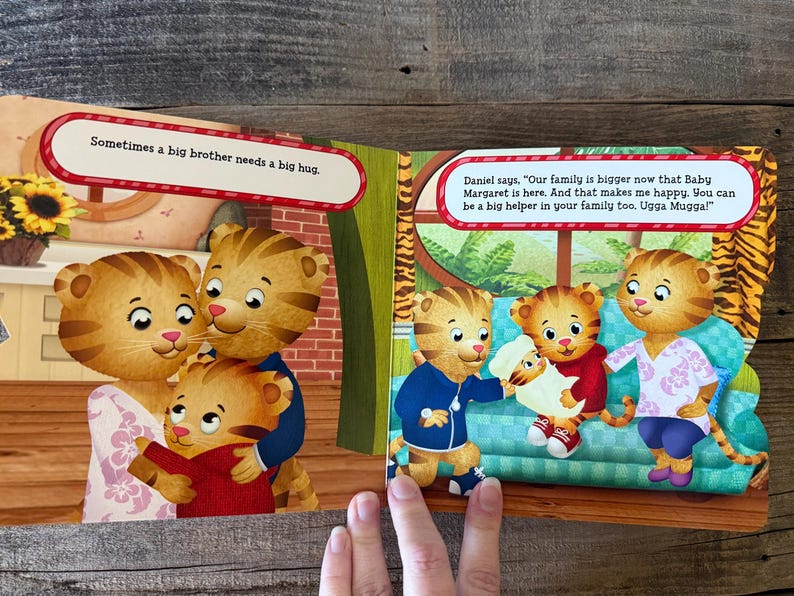 Puede incluir: Ilustraci&oacute;n de libro infantil con personajes de Daniel el Tigre. La p&aacute;gina izquierda muestra a una familia abraz&aacute;ndose, con el texto: &laquo;A veces un hermano mayor necesita un gran abrazo&raquo;. La p&aacute;gina derecha muestra a Daniel el Tigre con su familia.