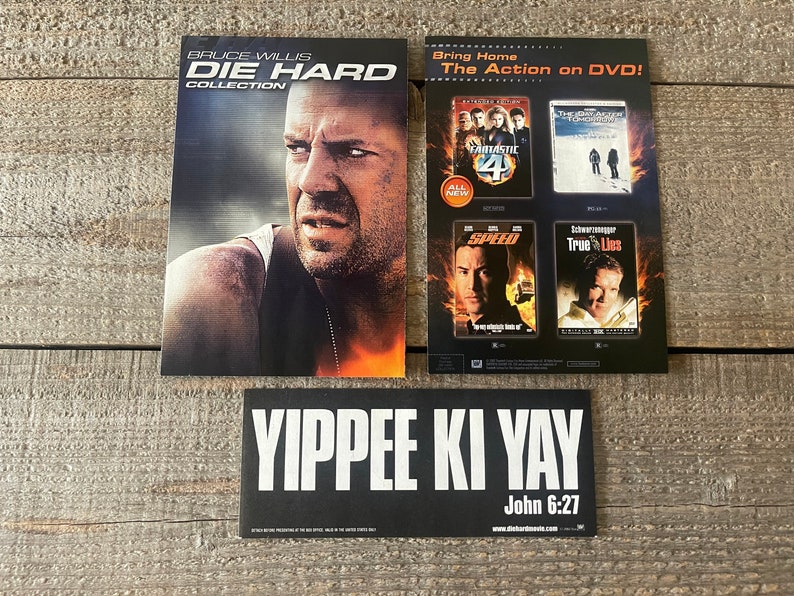 K&ouml;nnte beinhalten: Ein schwarz-wei&szlig;er Aufkleber mit dem Text "YIPPEE KI YAY" und "John 6:27" in wei&szlig;er Schrift. Der Aufkleber wirbt f&uuml;r die "Die Hard Collection" auf DVD. Das Bild zeigt auch ein DVD-Cover mit Bruce Willis als John McClane aus dem Film "Die Hard".