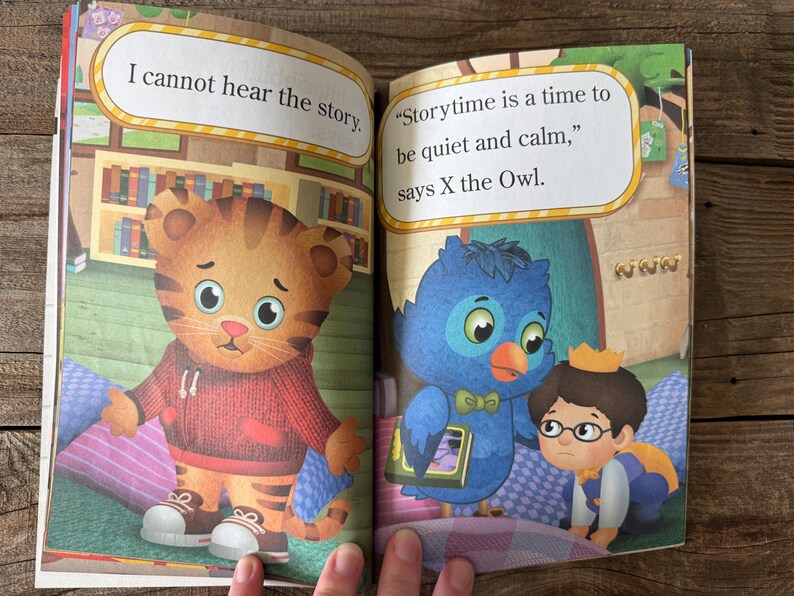 May include: A children's book spread featuring illustrations of cartoon characters. One page shows a tiger-like character with the text "I cannot hear the story." The other page shows an owl and a boy with the text "Storytime is a time to be quiet and calm."