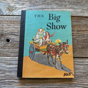 May include: Vintage children's book titled "The Big Show." The cover features a colorful illustration of a clown and a girl in a cart pulled by a donkey. The book has a teal background with the title in large white letters.