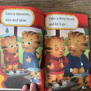 May include: A children's book spread featuring illustrations of Daniel Tiger. The left page reads "Give a squeeze, nice and slow." The right page reads "Take a deep breath and let it go."
