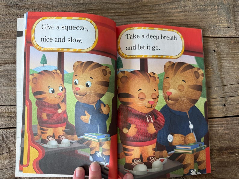 May include: A children's book spread featuring illustrations of Daniel Tiger. The left page reads "Give a squeeze, nice and slow." The right page reads "Take a deep breath and let it go."