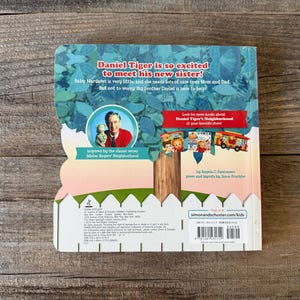 Puede incluir: Un libro infantil con una portada azul y blanca con el texto "&iexcl;Daniel Tiger est&aacute; tan emocionado de conocer a su nueva hermana!" y una ilustraci&oacute;n de Daniel Tiger. El libro est&aacute; inspirado en Mister Rogers' Neighborhood.