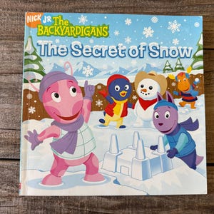 Puede incluir: Portada del libro infantil "El Secreto de la Nieve" con los personajes de Backyardigans. La portada es predominantemente azul y blanca, que representa una escena de nieve con personajes de dibujos animados, un muñeco de nieve y un fuerte de nieve.