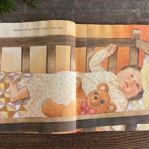 Pu&ograve; includere: Una bambina dorme in una culla di legno con un orsacchiotto. La culla ha una trapunta bianca e marrone. Il testo "Melissa was the Brown family's new baby." &egrave; visibile sulla pagina.
