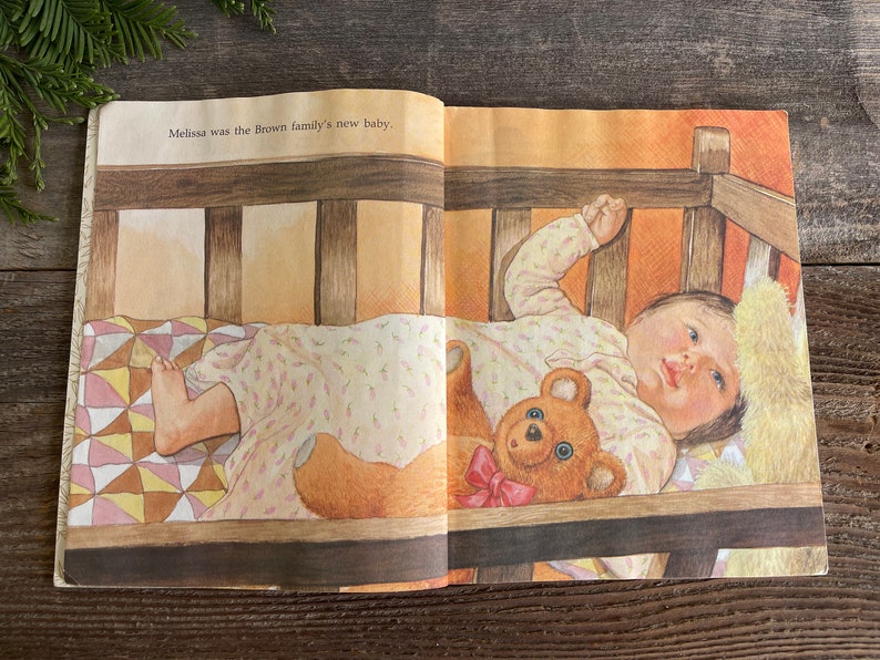 Pu&ograve; includere: Una bambina dorme in una culla di legno con un orsacchiotto. La culla ha una trapunta bianca e marrone. Il testo "Melissa was the Brown family's new baby." &egrave; visibile sulla pagina.