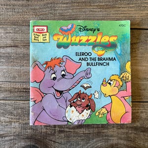 Könnte beinhalten: Ein Vintage-Disney's Wuzzles Buch- und Kassetten-Set. Das Cover zeigt Illustrationen der Zeichentrickfiguren Eleroo und Brahma Bullfinch. Das Buch ist grün mit blauem Hintergrund und dem Text "24 Page Book Read Along Tape".