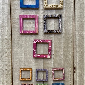 May include: A collection of ten small, square picture frames with various colorful patterns and designs. The frames are made of wood and have a rustic, handmade look.