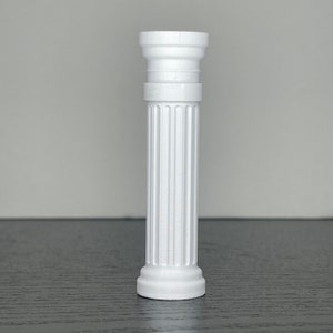 May include: A white, miniature, fluted column with a detailed capital and base. The column is made of a solid material and stands upright against a neutral background. The column is approximately 6 inches tall.