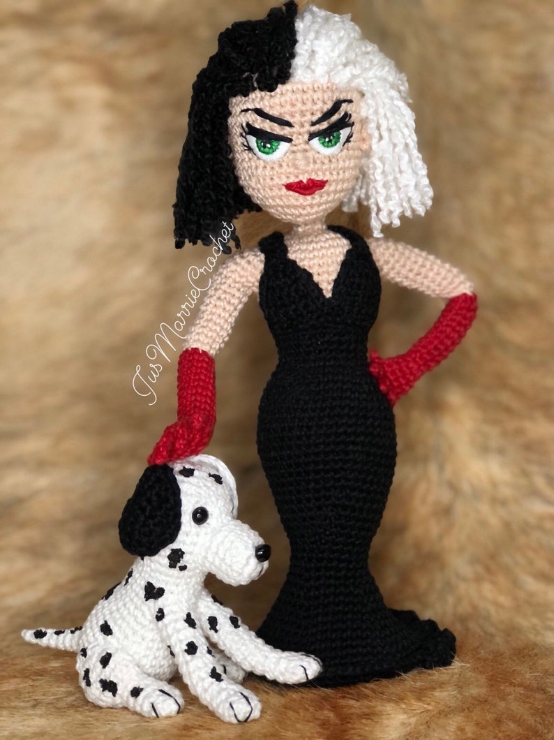 May include: A crocheted doll of Cruella de Vil from Disney's 101 Dalmatians, wearing a black dress and red gloves, standing next to a crocheted Dalmatian puppy.