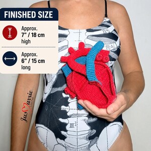 May include: A crocheted anatomical heart model in red and blue yarn. The text FINISHED SIZE indicates a height of approximately 7 inches and a length of approximately 6 inches. The heart is held against a black and white skeleton print bodysuit.