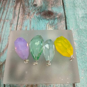 Puede incluir: Cuatro colgantes de cristal facetados en varios colores, incluyendo morado, verde, azul claro y amarillo. Cada colgante tiene un lazo plateado para sujetarlo a un collar o pulsera.