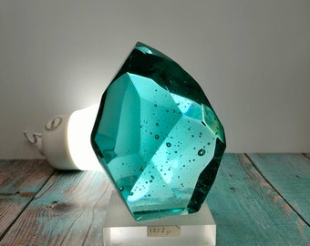 Peut inclure: Une sculpture en verre bleu turquoise avec un design facetté et des bulles d'air. La sculpture est sur un piédestal blanc avec le texte "1558" dessus.