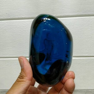 May include: A smooth, dark blue glass paperweight with swirling patterns inside. The paperweight is shaped like a rounded oval.