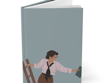 May include: A hardbound journal with a light blue cover featuring an illustration of a woman in a pink and white striped shirt, brown skirt, and black tie, holding a tablet and standing near a ladder. The journal's pages are white.