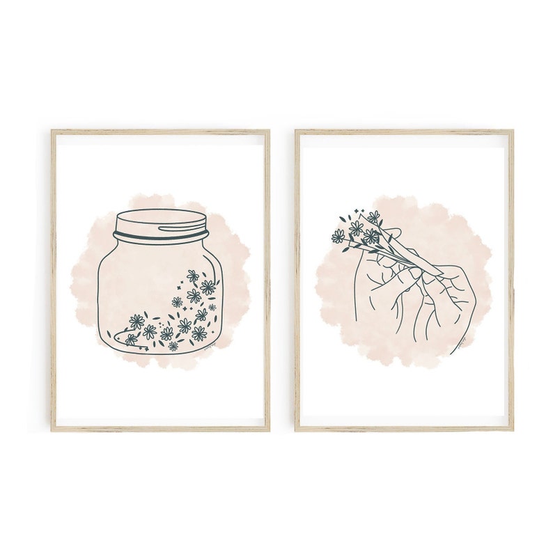 May include: Two framed art prints. One features a jar with flowers, the other shows a hand holding flowers. Both have a light pink watercolor background and dark teal line art. The frames are light wood.