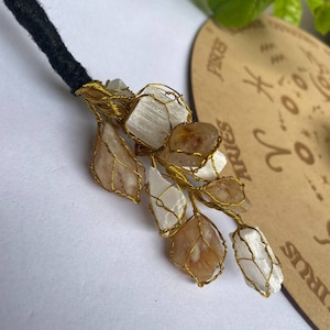 May include: A gold wire wrapped crystal tree with white and brown crystals. The tree is attached to a black cord.