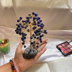 May include: A gold wire tree sculpture with blue glass beads, each bead has a white eye design. The tree is sitting on a grey rock base.