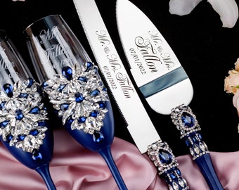May include: A wedding cake cutting set with two blue and crystal embellished champagne flutes and a silver cake knife with a blue handle. The knife is engraved with "Mr. & Mrs. Tallon 07.01.2022".