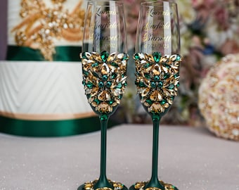 May include: Two emerald green champagne flutes with gold and green rhinestones, decorated with the names Lorraine & Garfield Barnett and the date 07/23/2023.